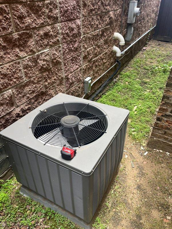 Conducted AC estimate for heat pump replacement system serving first floor and basement. Existing air conditioning condenser unit is 15-20 years old and existing furnace is approximately 14 years old. Inspected outdoor condensing unit positioned on concrete pad in narrow side yard service area between buildings. Unit shows age-appropriate wear with visible weathering on surrounding brick structure and moisture accumulation evidenced by moss growth at wall base. Documented existing electrical junction boxes, PVC condensate drainage system, and current equipment configuration. Assessed installation space constraints due to narrow alleyway access and proximity to brick walls. Photographed existing equipment and site conditions for replacement system planning.