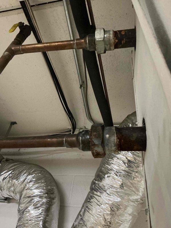 Responded to commercial facility for reported leak at lobby air handler system. Upon inspection, identified active leak at corroded galvanized steel union fittings connecting copper refrigerant lines. Evidence of significant water damage and mold growth on surrounding wall surfaces indicated leak had been present for extended period. Replaced failed union fittings with new brass compression fittings to restore system integrity. Tested all connections for proper seal and verified no additional leaks present. System returned to normal operation. Documented conditions with photos showing before state of corroded fittings and water damage for facility records.