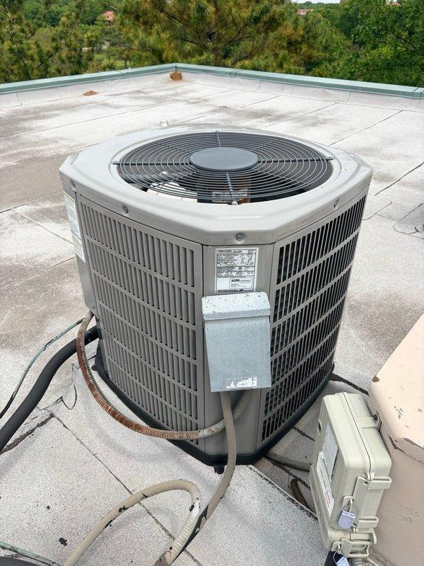 Completed comprehensive tune-up service on a rooftop-mounted cylindrical air conditioning condenser unit. Performed standard maintenance procedures including inspection of electrical components, contactor operation, and refrigerant line connections. Noted deteriorated wire insulation on yellow-striped conductors within the control panel, indicating age-related wear requiring future attention. All system components operational at time of service completion, with photographic documentation captured for service records.