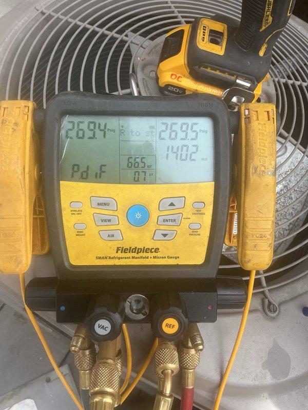 Installed Luxaire outdoor condenser unit on concrete pad beneath deck structure. Positioned equipment, completed electrical disconnect connections, and installed refrigerant linesets. Performed initial pressure testing using manifold gauges, recording operating pressures of 263.4 PSI high side and 120.5 PSI low side with ambient temperatures monitored during startup verification.