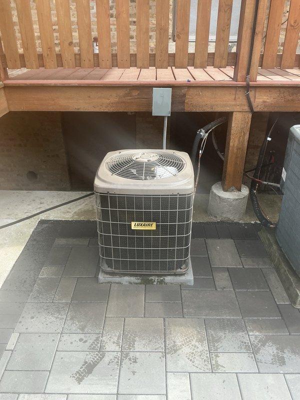 Installed Luxaire outdoor condenser unit on concrete pad beneath deck structure. Positioned equipment, completed electrical disconnect connections, and installed refrigerant linesets. Performed initial pressure testing using manifold gauges, recording operating pressures of 263.4 PSI high side and 120.5 PSI low side with ambient temperatures monitored during startup verification.