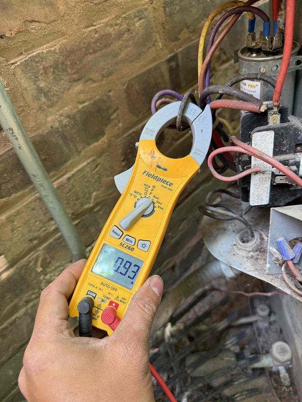 Responded to service call for air conditioning unit producing loud rattling noise during startup. Upon arrival, performed diagnostic inspection of outdoor condensing unit and electrical components. Measured electrical current draw using clamp meter, which showed readings within normal operating range at 0.93 amps. Conducted thorough visual and auditory inspection of compressor, fan motor, mounting hardware, and capacitor assembly. Inspected all electrical connections, wire terminals, and capacitor for signs of loose components or deterioration. Unit was operational and providing adequate cooling at time of inspection. Documented equipment condition with photos showing electrical measurements and component assembly. Noise concern noted but unit functioning properly during diagnostic period.