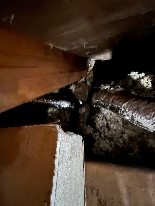Continued installation of Unico high-velocity HVAC system, including routing and securing flexible ductwork through crawl space with proper insulation wrapping. Installed and positioned ceiling-mounted supply outlets with chrome trim rings in bathroom area, completing system distribution for conditioned air delivery.