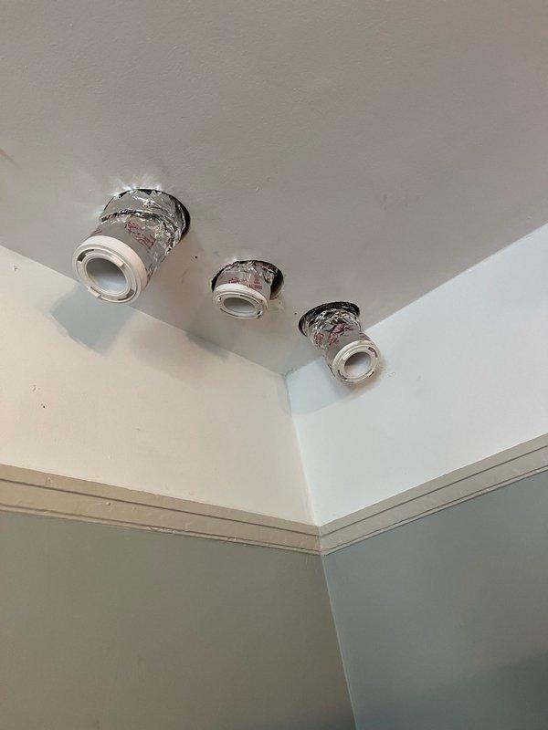 Continued installation of Unico high-velocity HVAC system, including routing and securing flexible ductwork through crawl space with proper insulation wrapping. Installed and positioned ceiling-mounted supply outlets with chrome trim rings in bathroom area, completing system distribution for conditioned air delivery.