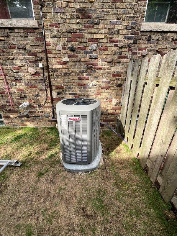 Continued and completed high velocity HVAC system installation at residential property. Installed Lennox outdoor condensing unit on concrete pad in side yard between brick exterior wall and privacy fence, connected refrigerant lines with proper insulation (black foam and blue covering), and routed lines along fence structure. System positioned for optimal airflow and serviceability in confined space, with all refrigerant piping secured and electrical connections completed per manufacturer specifications.