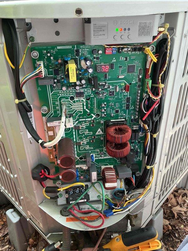 Performed comprehensive clean and check maintenance on Bosch air conditioning system per Comfort Plan agreement. Inspected outdoor condensing unit including condenser coil, fan motor operation, and electrical components. Accessed control board and verified all electronic components, including toroidal inductors, capacitors, and digital display functioning properly at 8.8 reading. Checked all wire connections, terminal tightness, and control board indicators showing normal green and red LED status. Cleaned condenser coil, inspected fan blade assembly and grille guard, verified proper drainage, and confirmed refrigerant levels within manufacturer specifications. Unit operating efficiently with no deficiencies noted.