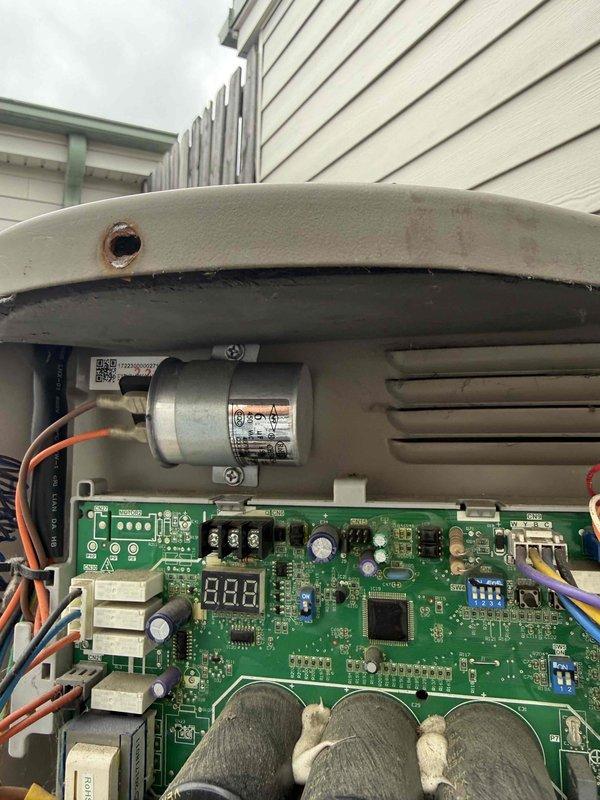 Replaced failed 6 microfarad capacitor in Bosch air conditioning unit. Tested new capacitor with digital meter to verify proper electrical specifications and confirmed system operation. Documented installation with photos showing capacitor testing and final placement on control board.