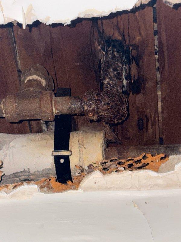 Responded to water leak in bathroom related to heating system piping. Created ceiling access point to locate and assess leak source. Upon inspection, discovered compromised galvanized pipe penetrating through wall structure with evidence of significant water damage to surrounding building materials, including deteriorated framing and visible moisture staining. Repaired leaking pipe connection and secured affected area. Documented extensive pre-existing fire and water damage to wall cavity for property management review.