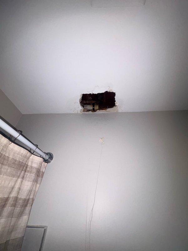 Responded to water leak in bathroom related to heating system piping. Created ceiling access point to locate and assess leak source. Upon inspection, discovered compromised galvanized pipe penetrating through wall structure with evidence of significant water damage to surrounding building materials, including deteriorated framing and visible moisture staining. Repaired leaking pipe connection and secured affected area. Documented extensive pre-existing fire and water damage to wall cavity for property management review.