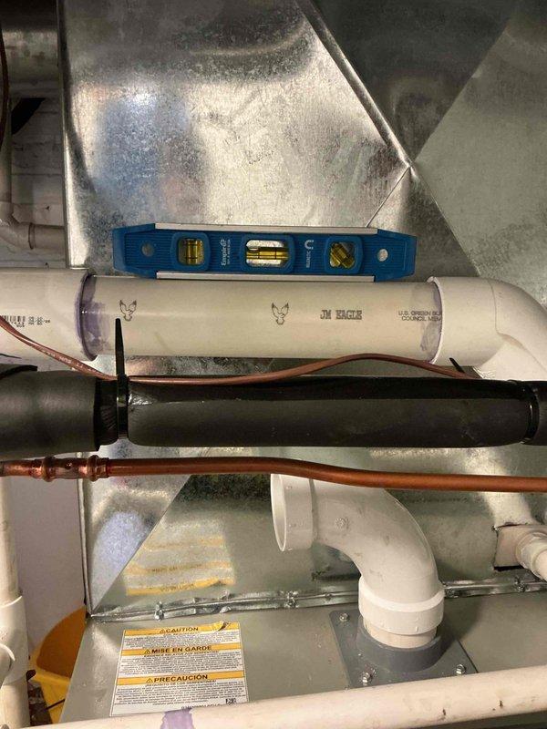 Completed installation of 2-inch PVC flue pipe exhaust system for residential HVAC unit. Installed horizontal exhaust piping with proper pitch and alignment, verified with level to ensure correct drainage and venting. Connected white PVC piping to green furnace unit with appropriate fittings and elbows, integrating with existing condensate drainage system. All connections properly secured and tested for proper exhaust ventilation in accordance with manufacturer specifications and local building codes.