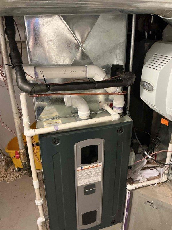 Completed installation of 2-inch PVC flue pipe exhaust system for residential HVAC unit. Installed horizontal exhaust piping with proper pitch and alignment, verified with level to ensure correct drainage and venting. Connected white PVC piping to green furnace unit with appropriate fittings and elbows, integrating with existing condensate drainage system. All connections properly secured and tested for proper exhaust ventilation in accordance with manufacturer specifications and local building codes.