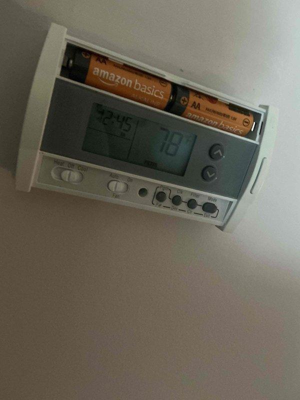 Responded to no cooling call at a converted 2-flat with rooftop HVAC unit accessed through interior roof opening. Upon arrival, found thermostat displaying 78°F set point with 45°F actual temperature reading and open battery compartment with depleted batteries. Inspected rooftop condensing unit showing signs of age with weathered components and multiple electrical connections. Identified low battery condition preventing proper thermostat operation and communication with cooling system. Replaced batteries in thermostat to restore power and proper function. Verified thermostat display operational and system able to call for cooling. Unit restored to normal operation with proper temperature control capability.