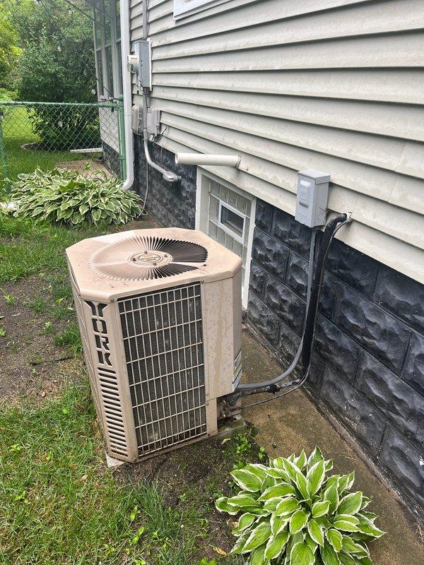Completed full HVAC system replacement for residential property with 18-19 year old underperforming equipment. Removed existing furnace and air conditioning system and installed new York condenser unit on exterior concrete pad with proper refrigerant line set routing along foundation and up siding. Installed new indoor air handler in basement utility area with updated galvanized ductwork connections. Completed all necessary piping connections including copper refrigerant lines, PVC condensate drainage, and electrical disconnect installation. System tested and operational upon completion.