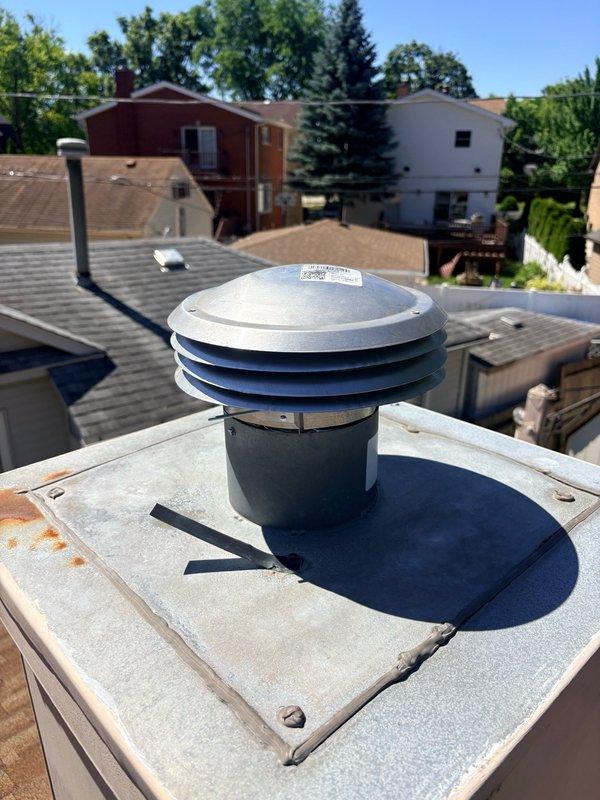 Replaced deteriorated chimney cap with new blue cylindrical cap featuring multi-tiered stainless steel dome top to prevent water intrusion and ensure proper ventilation. Installed unit securely on existing white masonry chimney base with weather-resistant mounting to protect flue system from the elements.