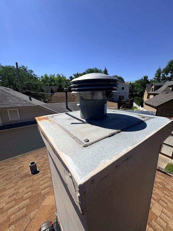Replaced deteriorated chimney cap with new blue cylindrical cap featuring multi-tiered stainless steel dome top to prevent water intrusion and ensure proper ventilation. Installed unit securely on existing white masonry chimney base with weather-resistant mounting to protect flue system from the elements.