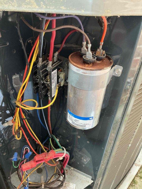 Performed warranty inspection on outdoor HVAC unit. Accessed interior compartment and identified heavily corroded capacitor with significant rust on top cap and terminals. Evaluated electrical connections and wiring configuration throughout unit, noting multiple wire bundles secured with proper routing. Used digital multimeter to test capacitor functionality, obtaining diagnostic readings to determine component condition. Documented unit condition with photographs showing weathered components consistent with extended outdoor exposure. Prepared to return with blower motor for potential warranty replacement if needed, pending further diagnostic evaluation and concurrent preventative maintenance service.