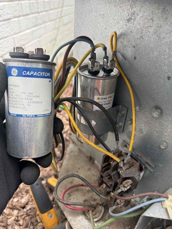 Responded to no cooling call on outdoor HVAC unit. Upon arrival, performed electrical diagnostics using clamp meter to measure amperage draw and verify compressor operation. Inspected outdoor condensing unit components including dual capacitors (GE and TITAN PRO brands) and contactor assembly. Found 12.9 amp reading during testing, indicating potential issue with compressor or capacitor performance. Evaluated all electrical connections, wiring integrity, and component conditions to determine root cause of cooling failure.
