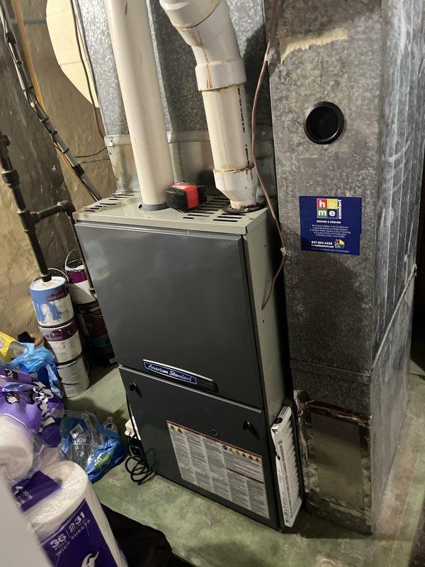 Conducted comprehensive assessment of 17-year-old Comfort Maker air conditioning system located in backyard area. Unit remains operational despite age. Evaluated outdoor condensing unit positioned against building exterior, partially screened by landscaping including hostas and ornamental shrubs. Inspected indoor furnace and air handler system in basement mechanical room, noting proper PVC venting configuration and drainage lines. Documented current system condition through photographic evidence of both indoor and outdoor components. Provided estimate for replacement air conditioning system with available promotional discount to address aging equipment and improve energy efficiency.