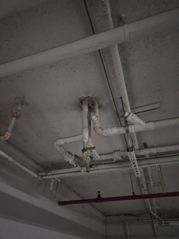 Responded to water leak service call in underground parking garage facility. Upon arrival, inspected overhead plumbing infrastructure including white-painted distribution lines, support brackets, and yellow valve assembly mounted to concrete ceiling. Observed moisture staining and discoloration on concrete surfaces indicating previous or active water intrusion. Documented existing conditions of exposed piping network, mechanical systems, and ceiling-mounted utilities for service records. Collected standard dispatch fee and discussed available repair options with property representative.