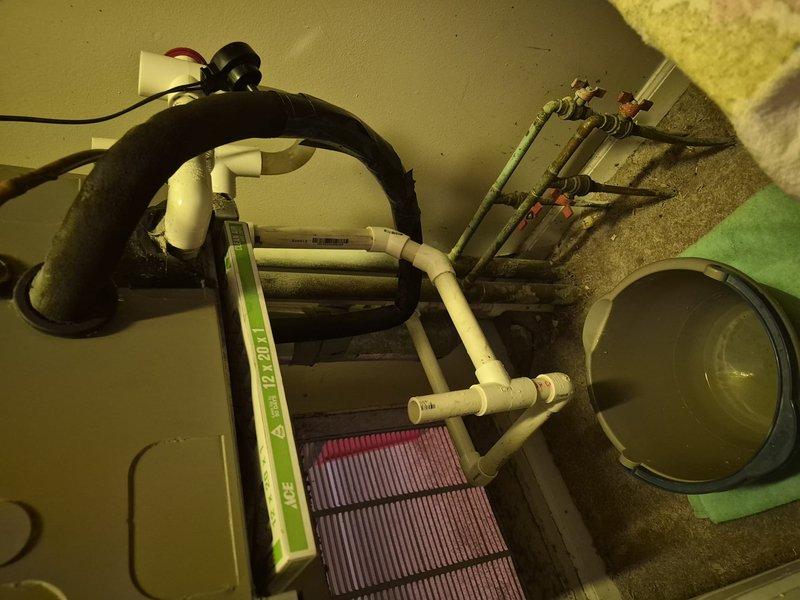 Responded to water leak call at commercial HVAC installation. Upon inspection, identified active leak at evaporator coil assembly with water collecting in green bucket placed on floor beneath unit. Assessed PVC condensate drain piping and connections for proper flow and potential blockages. Examined corroded metal piping components and fittings in system, noting deterioration that may have contributed to leak condition. Checked flexible duct connections and refrigerant line integrity. Documented equipment condition including coil assembly, drain pan, and associated plumbing components with photographs for service records.