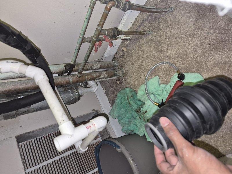 Responded to water leak call at commercial HVAC installation. Upon inspection, identified active leak at evaporator coil assembly with water collecting in green bucket placed on floor beneath unit. Assessed PVC condensate drain piping and connections for proper flow and potential blockages. Examined corroded metal piping components and fittings in system, noting deterioration that may have contributed to leak condition. Checked flexible duct connections and refrigerant line integrity. Documented equipment condition including coil assembly, drain pan, and associated plumbing components with photographs for service records.