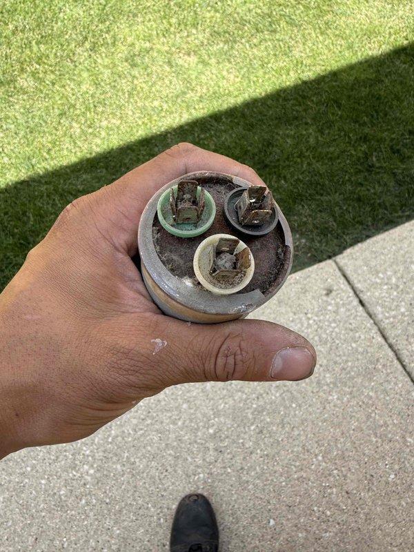 Responded to no cooling complaint on residential air conditioning system. Upon arrival, verified compressor was not engaging and performed diagnostic testing on outdoor condensing unit. Identified failed dual run capacitor exhibiting severe corrosion and terminal deterioration. Removed defective capacitor and tested electrical connections to confirm proper voltage supply. Replaced failed capacitor with new component, restored system operation, and verified compressor engagement and proper cooling cycle functionality.
