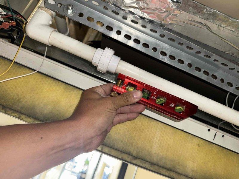 Responded to callback for recurring leak issue on commercial HVAC installation. Upon arrival, inspected PVC condensate drain line previously serviced and verified proper slope using torpedo level. Discovered accumulation of debris and mineral deposits at floor-level drain connection point indicating drainage system backup. Cleared blockage from drain line, cleaned connection fittings, and confirmed proper drainage flow to eliminate leak recurrence.