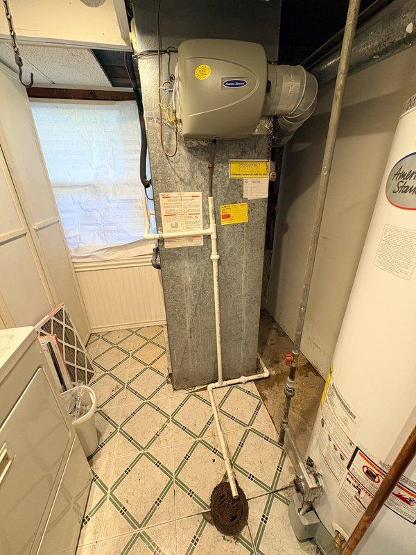 Responded to service call for air conditioning unit leaking water in basement utility area. Upon inspection, found humidifier mounted on gray metal ductwork above furnace air handler with visible moisture concerns. Assessed HVAC system for potential frozen evaporator coil condition as reported cause of water leak. Examined PVC condensate drain line routing and floor area showing evidence of water accumulation on tile flooring. Documented equipment conditions including humidifier unit, ductwork assembly, and drainage system configuration. Collected standard diagnostic fee and discussed available repair options with property owner, including preventive maintenance plan enrollment and new customer discount eligibility. Recorded all equipment model and specification information from existing labels on air handler and water heater for service records.
