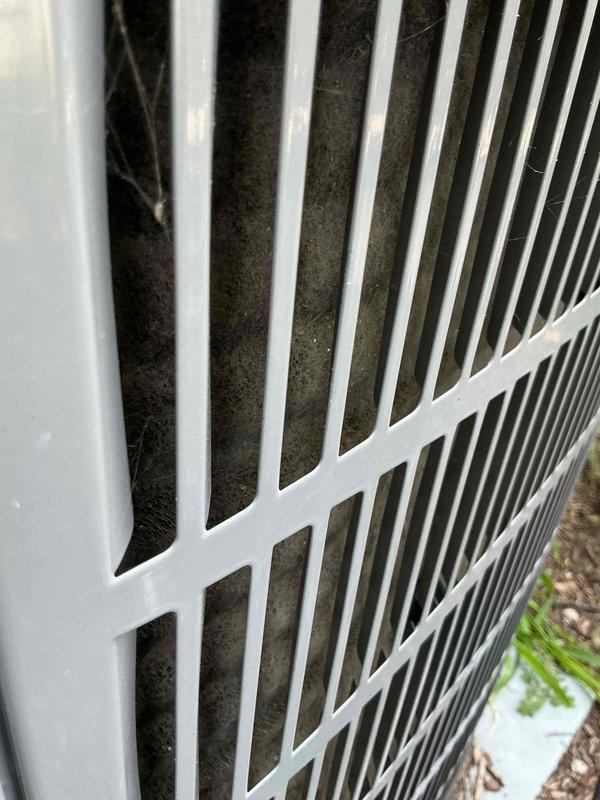 Responded to no cooling complaint on Bryant residential HVAC system less than five years old. Upon inspection, found outdoor condenser unit with heavily restricted airflow due to significant dust and debris accumulation on coil fins and grille openings. Documented equipment condition with photos showing utility closet installation and exterior unit with visible contamination blocking proper heat exchange. Diagnosed airflow restriction as primary cause of cooling failure and discussed cleaning requirements and maintenance recommendations with property owner to restore system performance.