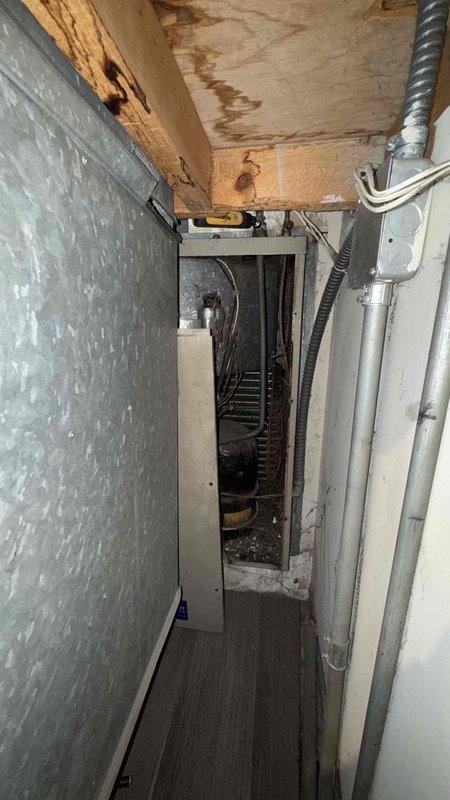 Responded to no cooling complaint for Singer AC unit model BCE22014. Upon arrival, inspected indoor evaporator coil assembly and refrigerant lines showing significant aging and oxidation on copper piping. Accessed air handler cabinet to evaluate internal components and refrigerant circuit. Observed water staining on ceiling near equipment indicating potential condensate drainage issues or previous leak history. Performed visual inspection of evaporator coil, refrigerant connections, and associated ductwork in confined utility space. Customer suspected low refrigerant charge as cause of insufficient cooling. Documented equipment condition with photos showing corroded copper lines, aged installation, and mechanical room configuration for diagnostic purposes and future service reference.