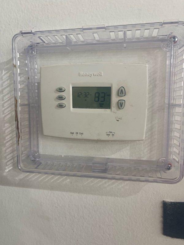 Responded to continued no cooling complaint in commercial office space on return visit. Upon arrival, verified thermostat settings and confirmed system was set to cooling mode with display reading 83°F. Performed diagnostic testing of air conditioning unit using clamp meter to measure electrical parameters at condenser coil. Observed evidence of corrosion and weathering on exterior housing panel and heat exchanger fins. Measured voltage reading of 225.8V at equipment. Documented thermostat operation with lockbox cover in place and captured electrical measurements during testing. Coordinated with office for approval process prior to proceeding with repairs, as tenant is responsible for HVAC maintenance at this property.