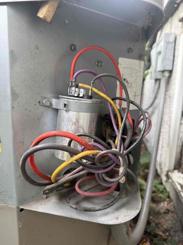 Responded to no cooling complaint on 10-15 year old residential air conditioning system. Upon arrival, performed visual inspection of outdoor condensing unit and electrical components. Accessed outdoor disconnect cabinet and observed weathered internal wiring and capacitor with signs of age-related deterioration including corrosion on cylindrical component surfaces. Utilized digital clamp meter to measure electrical parameters at the unit, obtaining amperage reading of 183.6 amps during diagnostic testing. Identified electrical issue preventing proper system operation. Documented equipment condition with photos showing internal cabinet components and diagnostic measurements. Presented repair options to restore cooling functionality.