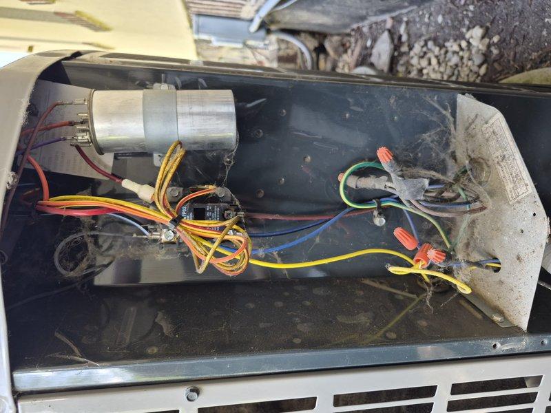 Responded to no-cooling call on residential HVAC system less than five years old. Upon arrival, performed visual inspection and diagnostic assessment of outdoor condensing unit. Removed access panel to examine electrical components and wiring connections. Found capacitor and associated wiring intact with proper connections secured by wire nuts. Identified significant deterioration and damage to condensate drain assembly, including cracked overflow safety switch housing with visible water damage and staining around the affected area. The broken drain pan fitting and compromised safety switch indicated previous water intrusion issues that likely triggered system shutdown as designed. Documented equipment condition through photography showing internal component layout, wiring configuration, damaged drain components, and surrounding corrosion. Explained findings to homeowner regarding the failed condensate management system and its impact on unit operation. Discussed repair options for rep