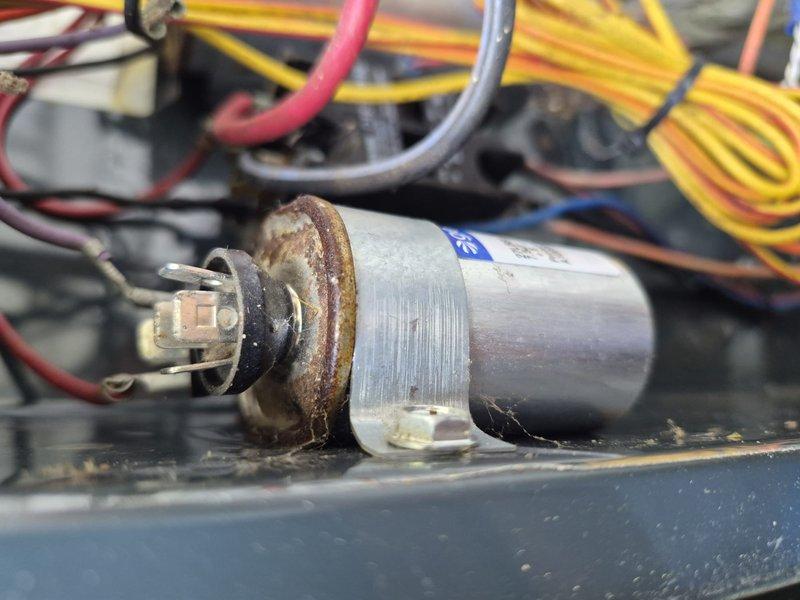 Responded to no cooling complaint on residential air conditioning system. Upon inspection, found failed dual-run capacitor with visible corrosion on mounting bracket and terminals. Capacitor tested below acceptable microfarad range, preventing compressor and condenser fan motor from operating properly. Replaced defective Genteq capacitor with new OEM-equivalent component, verified proper electrical connections, and tested system operation. Unit now cooling normally with compressor and outdoor fan motor running within manufacturer specifications.