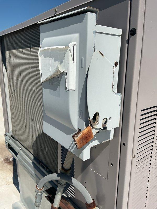 Responded to no cooling complaint for commercial office space. Upon arrival, found rooftop packaged HVAC unit with severely damaged electrical disconnect box. Disconnect cover was deteriorated with metal sections torn away, exposing internal components and creating safety hazard. Heavy rust observed on locking mechanism and mounting hardware. Inspected unit operation and refrigerant lines, which appeared intact. Documented equipment condition with photographs showing extent of disconnect box damage and overall unit status. Customer advised that comprehensive no cooling diagnostic was completed within past month. Collected continuation time for ongoing service issue related to inadequate cooling performance in office area.