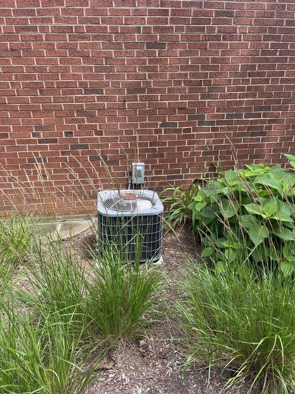 Responded to service call for non-operational air conditioning system affecting entire residence. Upon arrival, inspected 15-year-old outdoor condenser unit positioned against exterior brick wall. Unit showed signs of age and wear consistent with end-of-service-life equipment. Performed comprehensive system evaluation including visual inspection of condenser cabinet, protective grille, refrigerant line connections, and electrical disconnect. Assessed unit placement, clearance issues with surrounding vegetation growth, and overall installation conditions. Documented equipment age, model information, and current operating status through photographic documentation. Based on system age and operational assessment, provided detailed replacement estimate for new HVAC system installation to restore cooling functionality to the residence.
