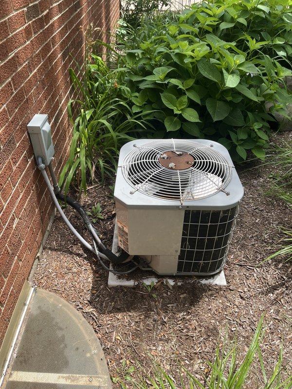 Responded to service call for non-operational air conditioning system affecting entire residence. Upon arrival, inspected 15-year-old outdoor condenser unit positioned against exterior brick wall. Unit showed signs of age and wear consistent with end-of-service-life equipment. Performed comprehensive system evaluation including visual inspection of condenser cabinet, protective grille, refrigerant line connections, and electrical disconnect. Assessed unit placement, clearance issues with surrounding vegetation growth, and overall installation conditions. Documented equipment age, model information, and current operating status through photographic documentation. Based on system age and operational assessment, provided detailed replacement estimate for new HVAC system installation to restore cooling functionality to the residence.