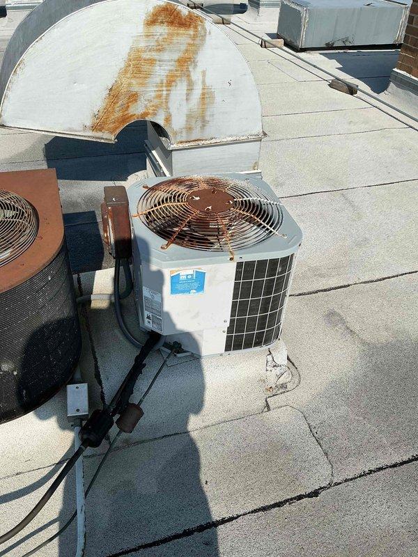 # HVAC Tune-Up Completed

Performed comprehensive tune-up on rooftop air conditioning system. Conducted electrical diagnostics using clamp meter, recording voltage and amperage readings to verify proper compressor operation at 303.1V and 13.001A. Inspected outdoor condensing unit, noting significant rust and corrosion on copper coil fins and aluminum fins throughout the unit, though system remained operational. Documented equipment condition including weathered exterior casing, deteriorated paint, and rust staining on associated metal housing panels. Verified refrigerant line connections and overall system functionality. Unit continues to operate despite visible aging and outdoor exposure damage.