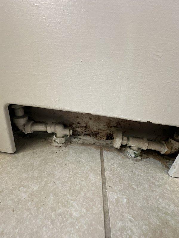 Conducted site assessment for boiler system estimate in older building with bathroom radiator installation. Documented existing conditions including access opening in first floor with exposed plumbing connections, two half-inch supply tubes extending from radiator unit, and layered flooring installation over original tile. Photographed significant mold growth on HVAC ductwork and ceiling surfaces indicating moisture intrusion issues, as well as plumbing access point showing discoloration and staining requiring attention during any future radiator work.