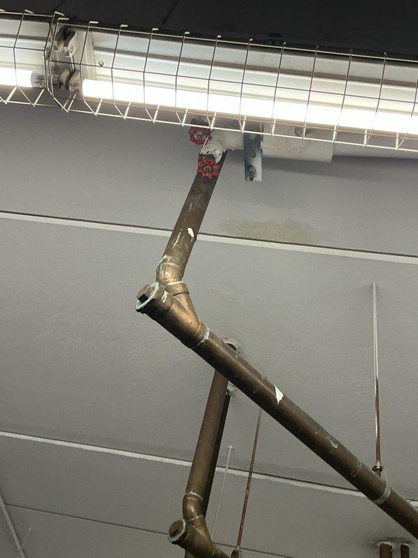Completed site inspection and documentation of ceiling-mounted refrigerant lines and associated plumbing infrastructure. Photographed copper refrigerant piping, manual shut-off valves, PVC drain lines, and mounting hardware to document current system configuration and condition for maintenance records.
