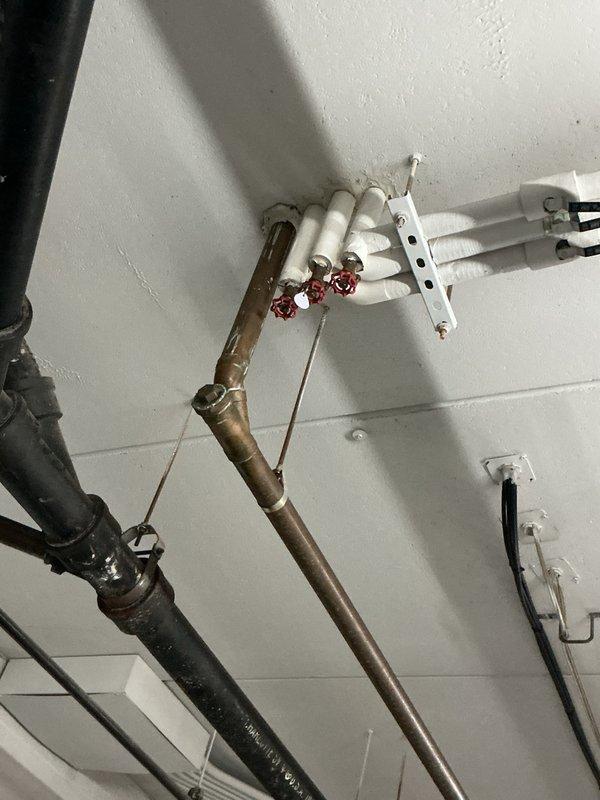 Completed site inspection and documentation of ceiling-mounted refrigerant lines and associated plumbing infrastructure. Photographed copper refrigerant piping, manual shut-off valves, PVC drain lines, and mounting hardware to document current system configuration and condition for maintenance records.