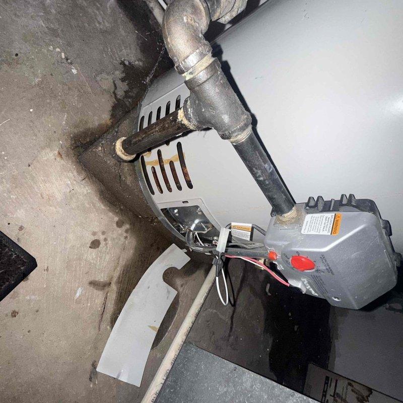 Responded to service call for leaking water heater. Upon arrival, performed comprehensive inspection of tanked water heater system and surrounding plumbing connections. Identified source of leak and assessed condition of unit, piping, and associated components. Documented equipment condition through photographs showing water heater installation, copper and galvanized piping connections, and evidence of moisture on concrete floor surface. Evaluated all pipe joints, fittings, and connections for integrity. Provided assessment and recommendations for necessary repairs to resolve active leak condition.