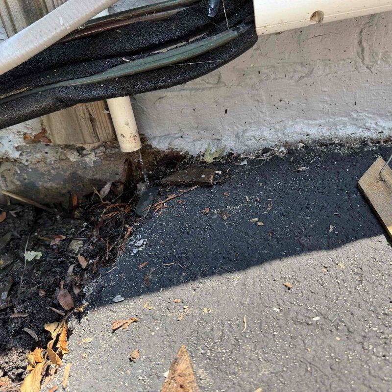 Responded to service call regarding reported system leak. Upon arrival, conducted thorough inspection of exterior condensate drainage system and refrigerant line set at foundation level. Located active leak at condensate drain line connection point where PVC T-fitting showed signs of moisture accumulation and improper drainage. Inspected insulated refrigerant lines for potential refrigerant leaks but found no evidence of refrigerant loss. Documented equipment information and photographed affected areas showing condensate drain configuration and line set installation at building foundation. Advised customer of findings and presented repair options to address condensate drainage issue and prevent future water damage.