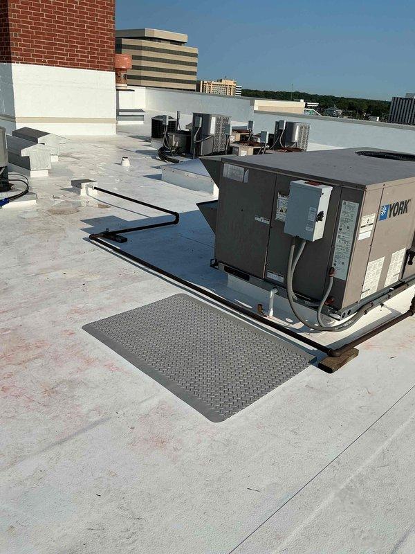 Conducted comprehensive rooftop inspection of multiple condensing units to assess electrical and mounting deficiencies. Documented deteriorated 30-year-old flexible electrical conduit whips and disconnect boxes that sustained wear during recent roof replacement project, requiring full replacement for all rooftop units. Identified numerous condensing units with inadequate support and improper mounting conditions resulting from equipment replacements over time. Photographed existing conditions including York-branded unit installations, corroded piping components, and missing equipment mounting pads. Recommended installation of plastic equipment pads where absent and correction of all mounting deficiencies to ensure proper equipment support and code compliance, with work scheduled for completion after cooling season.