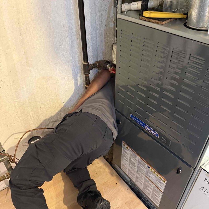 Responded to water leak complaint originating from American Standard furnace unit in basement. Upon inspection, identified moisture issue at HVAC equipment connections that customer had previously experienced approximately two months prior. Accessed components behind furnace unit to inspect copper piping connections and drain system. Examined condensate drainage system and associated PVC piping components on top of unit. Verified plumbing connections and inspected surrounding area including overhead black pipe joints and nearby water heater for potential leak sources. Documented equipment information and captured photographic evidence of work area and equipment condition for service records.