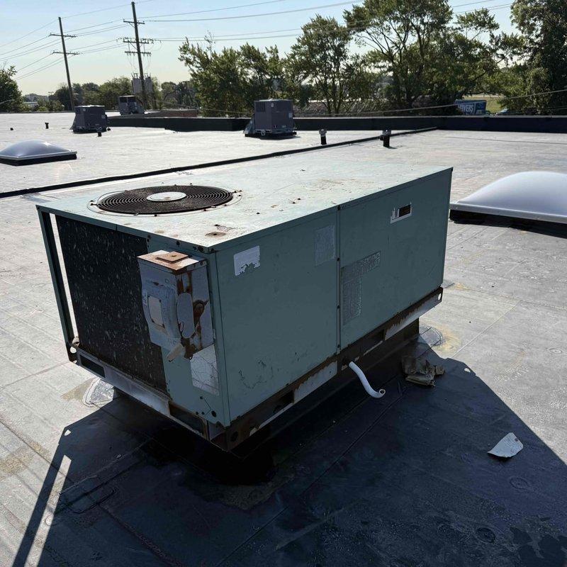 Responded to no cooling complaint for commercial rooftop package unit serving rear portion of building. Upon arrival, accessed rooftop HVAC system and performed visual inspection of weathered package unit showing significant age-related deterioration, surface rust on fan guard assembly, and corroded mounting hardware. Documented unit condition with photographs showing extensive rust around fan housing perimeter and compromised exterior finish. Coordinated key pickup and return, noted concurrent roofing work in progress on property.