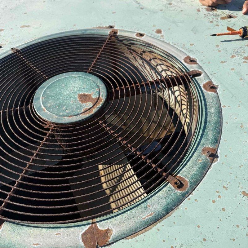 Responded to no cooling complaint for commercial rooftop package unit serving rear portion of building. Upon arrival, accessed rooftop HVAC system and performed visual inspection of weathered package unit showing significant age-related deterioration, surface rust on fan guard assembly, and corroded mounting hardware. Documented unit condition with photographs showing extensive rust around fan housing perimeter and compromised exterior finish. Coordinated key pickup and return, noted concurrent roofing work in progress on property.