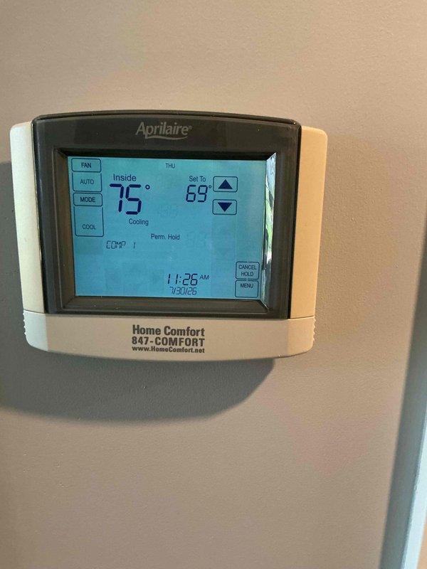 Responded to no cooling complaint on 10+ year old HVAC system where indoor temperature was rising to 75°F despite thermostat set to 69°F. Upon arrival, confirmed Aprilaire thermostat was properly set to cooling mode with permanent hold engaged, displaying 75°F actual temperature. Verified indoor blower motor was operating normally, but compressor was not engaging. Previous attempts to reset breaker and unit by building maintenance had not resolved the issue. Accessed HVAC equipment in utility closet and performed diagnostic evaluation of furnace and air conditioning components. Inspected electrical connections, copper refrigerant lines, and shut-off valves. Documented equipment model information and captured photos of thermostat display showing temperature differential and system configuration, as well as interior HVAC installation. Coordinated with office regarding condo association approval process for repairs per building policy. System requires compressor circuit diagnosis and pote