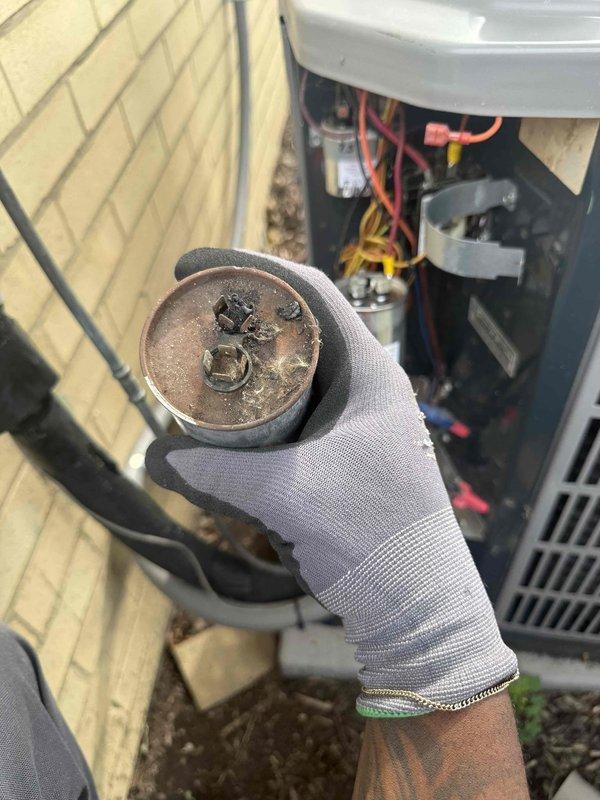Responded to service call for non-operational 10-year-old air conditioning system with malfunctioning thermostat displaying incorrect heat mode and temperature readings up to 86°F. Upon inspection of outdoor condensing unit, discovered failed dual-run capacitor exhibiting severe corrosion, heat damage, and deterioration on terminal connections. Removed defective capacitor and installed new TITAN PRO replacement capacitor, restoring proper electrical function to compressor and condenser fan motor. Completed clean and check maintenance procedures on both air conditioning condenser unit and air handler as required. System tested successfully with proper cooling operation restored and thermostat communication functioning correctly.