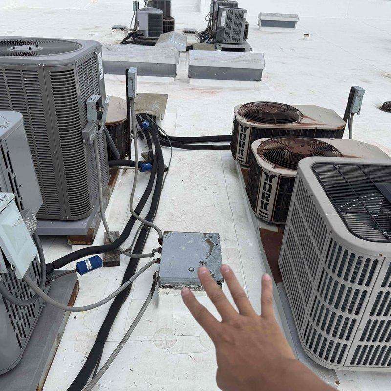 Conducted rooftop survey of commercial HVAC installation to identify air conditioning units operating without proper equipment pads. Inspected multiple condenser units of varying ages, including older cylindrical models and newer rectangular units, documenting equipment placement and support conditions. Photographed roof-mounted AC units, electrical disconnects, refrigerant line routing, and mounting configurations for assessment and future remediation planning.